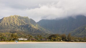 Una playa con una montaña al fondo, casas a lo largo de la orilla y un cielo despejado.
