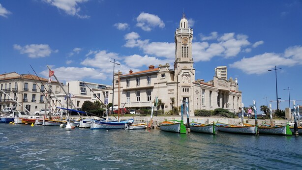A historic building with a clock tower, surrounded by a marina with several boats. - Le Repère de Charles Reboul, T3 (Marseillan)