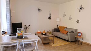 A modern living room with a dining area, featuring a sofa, coffee table, and a TV. - Le Repère de Charles Reboul, T3 (Marseillan)