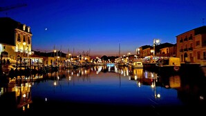 A marina at dusk with boats docked, calm water reflecting lights, and buildings along the waterfront. - Le Repère de Charles Reboul, T3 (Marseillan)