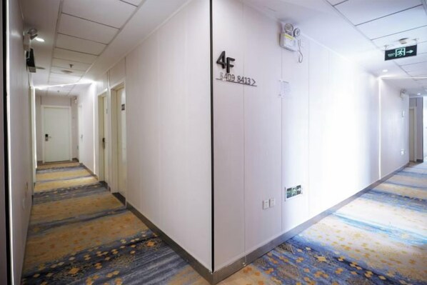 A hotel corridor with a carpeted floor, a door labeled '4F,' and a sign indicating the direction to the elevator. - Homeinn Pebble Hotel (Beijing West Railway Station South Square) (Beijing)