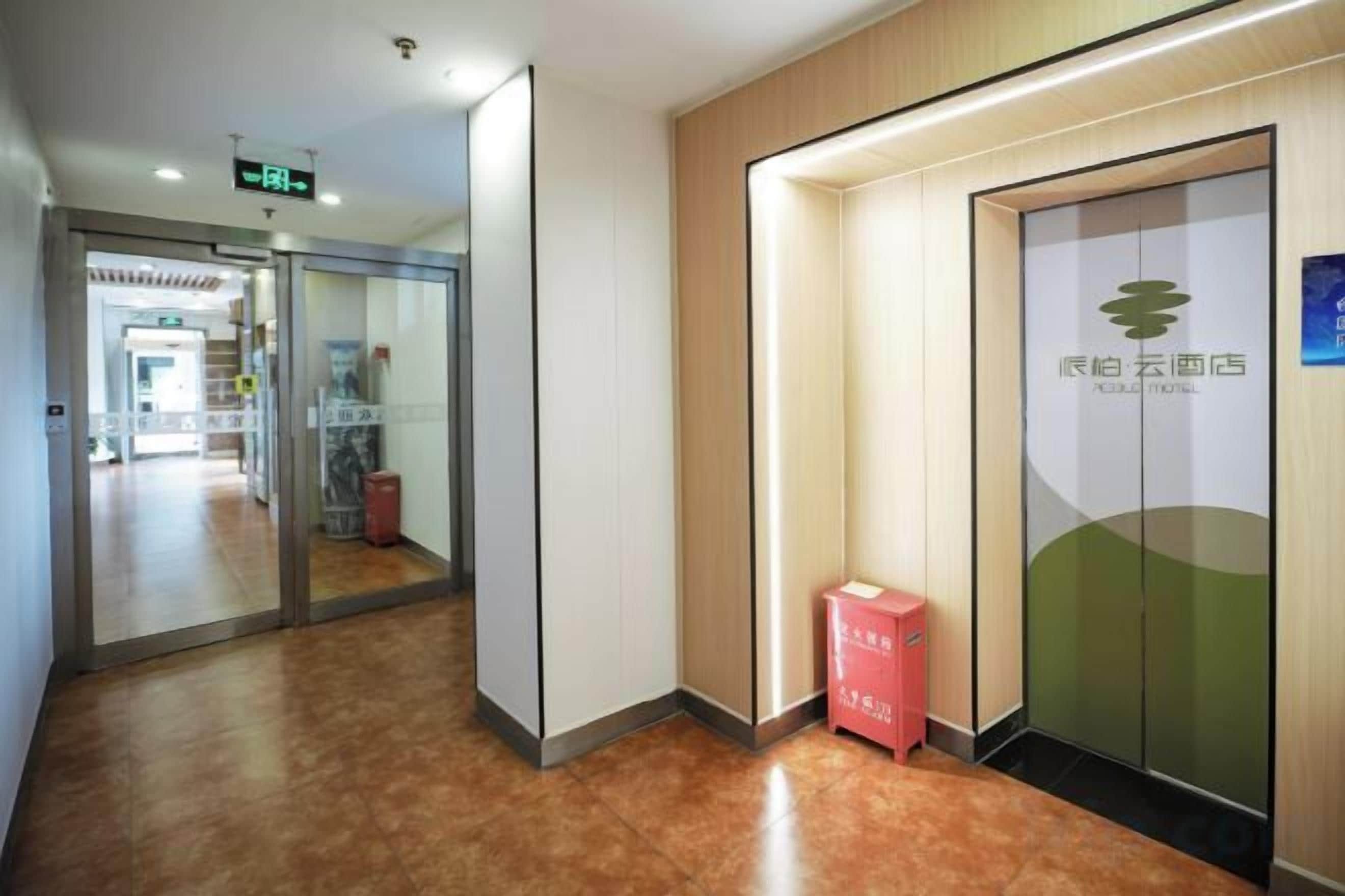 A hotel corridor with a reception area, a glass door with a logo, and a red box on the floor.