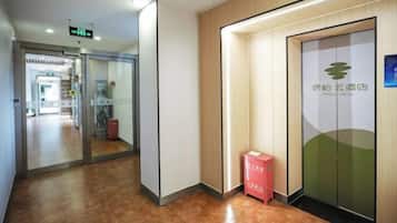 A hotel corridor with a reception area, a glass door with a logo, and a red box on the floor.