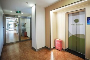 A hotel corridor with a reception area, a glass door with a logo, and a red box on the floor. - Homeinn Pebble Hotel (Beijing West Railway Station South Square) (Beijing)