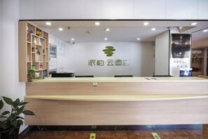 A reception desk with a logo, a counter, and a plant to the left. - Homeinn Pebble Hotel (Beijing West Railway Station South Square) (Beijing)