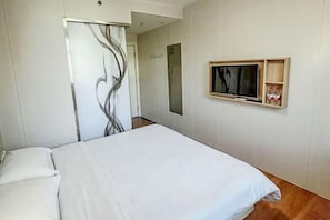 A hotel room with a bed, a TV mounted on the wall, and a wooden cabinet with bottles.