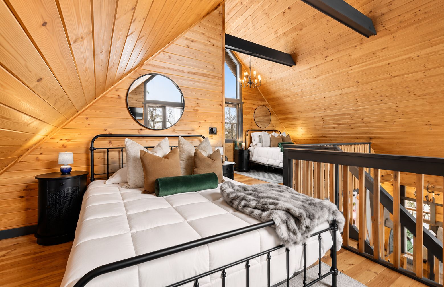 Een slaapkamer met een bed, kussens, een nachtkastje, een spiegel en uitzicht door een raam.