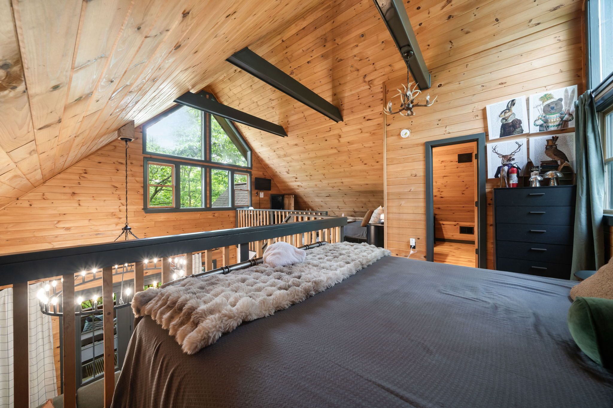 A wooden cabin bedroom with a bed, a window, a dresser, and a door.