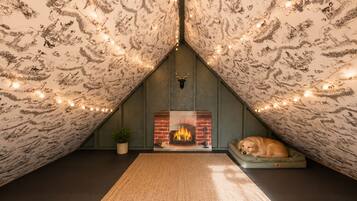 Een zolderkamer met een open haard, een hond die op een bank rust, en sfeerverlichting.