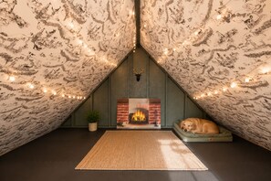 An attic room with a fireplace, a dog resting on a couch, and string lights. - Escape to our luxe, pet-friendly Blue Ridge cabin—sleeps 14 with top amenities! (Blue Ridge)