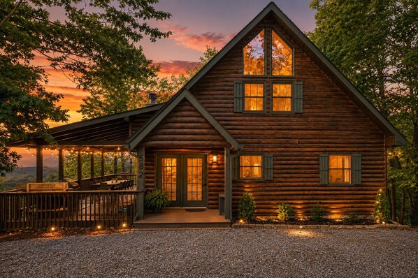 A log cabin with a porch, a deck, and a view of the landscape.