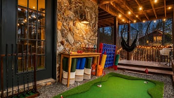 A cozy indoor mini-golf setup with a stone wall, wooden beams, and a small pool table.