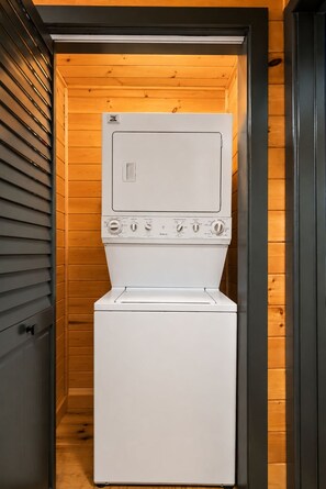 Een wit was- en droogcombivoor een kamer met houten wanden en een zwarte deur.