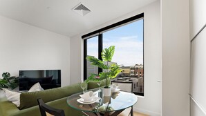 Un salon moderne avec une table à manger en verre, un canapé vert et une grande fenêtre donnant sur la ville.