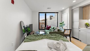 Une chambre d’hôtel moderne comprenant un lit, un petit coin salon, une vue sur la ville et une kitchenette.