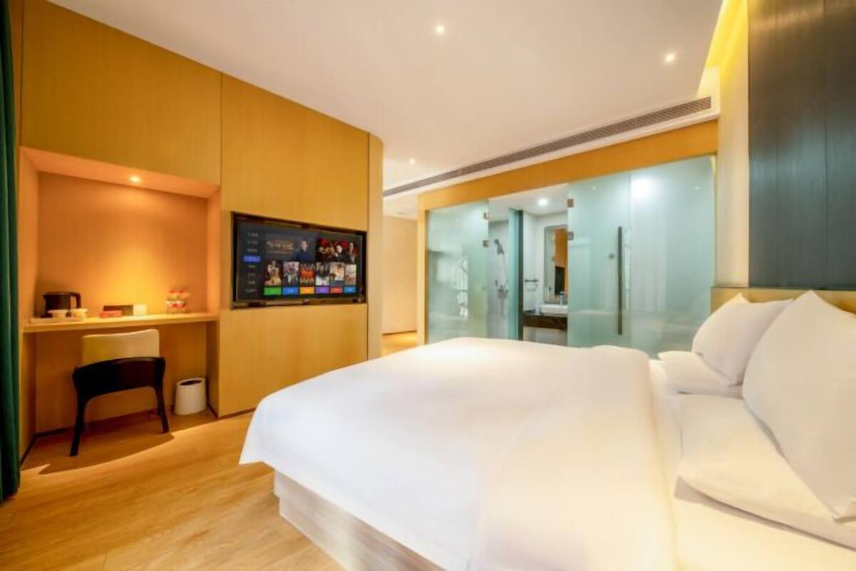 Habitación de hotel con cama, escritorio con computadora, una silla y televisor montado en la pared.