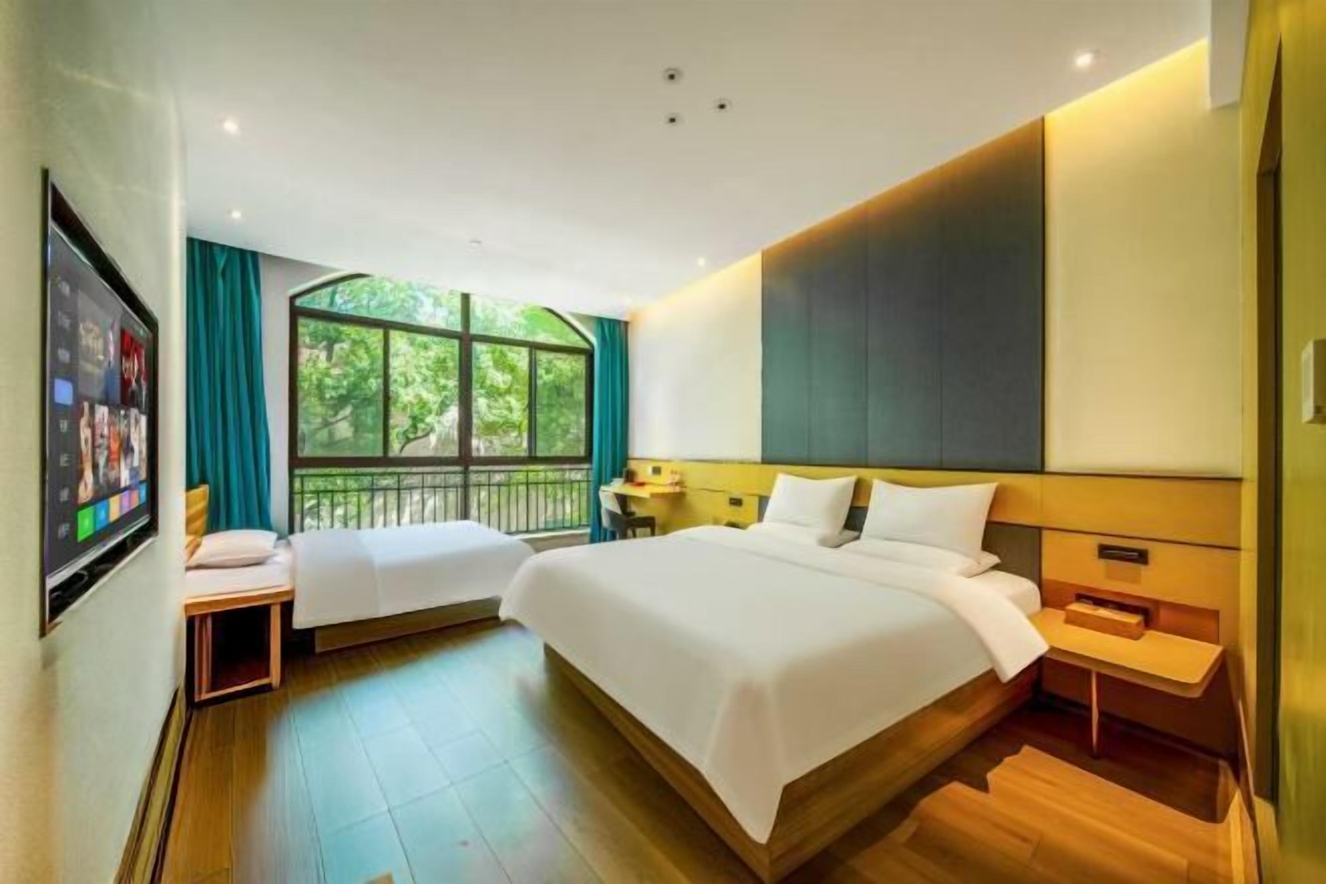 Habitación de hotel con dos camas, televisor, ventana con vista a vegetación y una mesita.