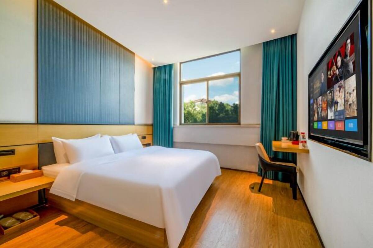 Una habitación de hotel con una cama grande, un escritorio, un televisor y una ventana con cortinas.