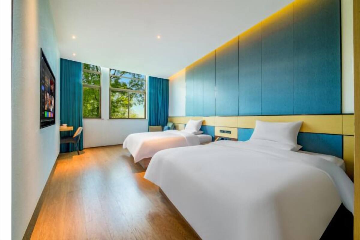 Habitación de hotel con dos camas, televisión y ventanas amplias con cortinas.