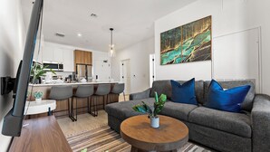 Uma sala de estar moderna com um sofá cinzento, almofadas azuis, uma mesa de centro redonda e um grande quadro abstrato na parede.