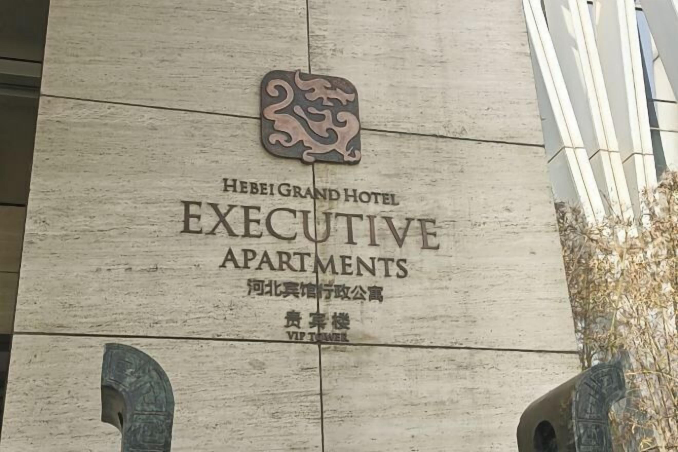 A sign for Hebei Grand Hotel Executive Apartments with a logo and name in both English and Chinese.