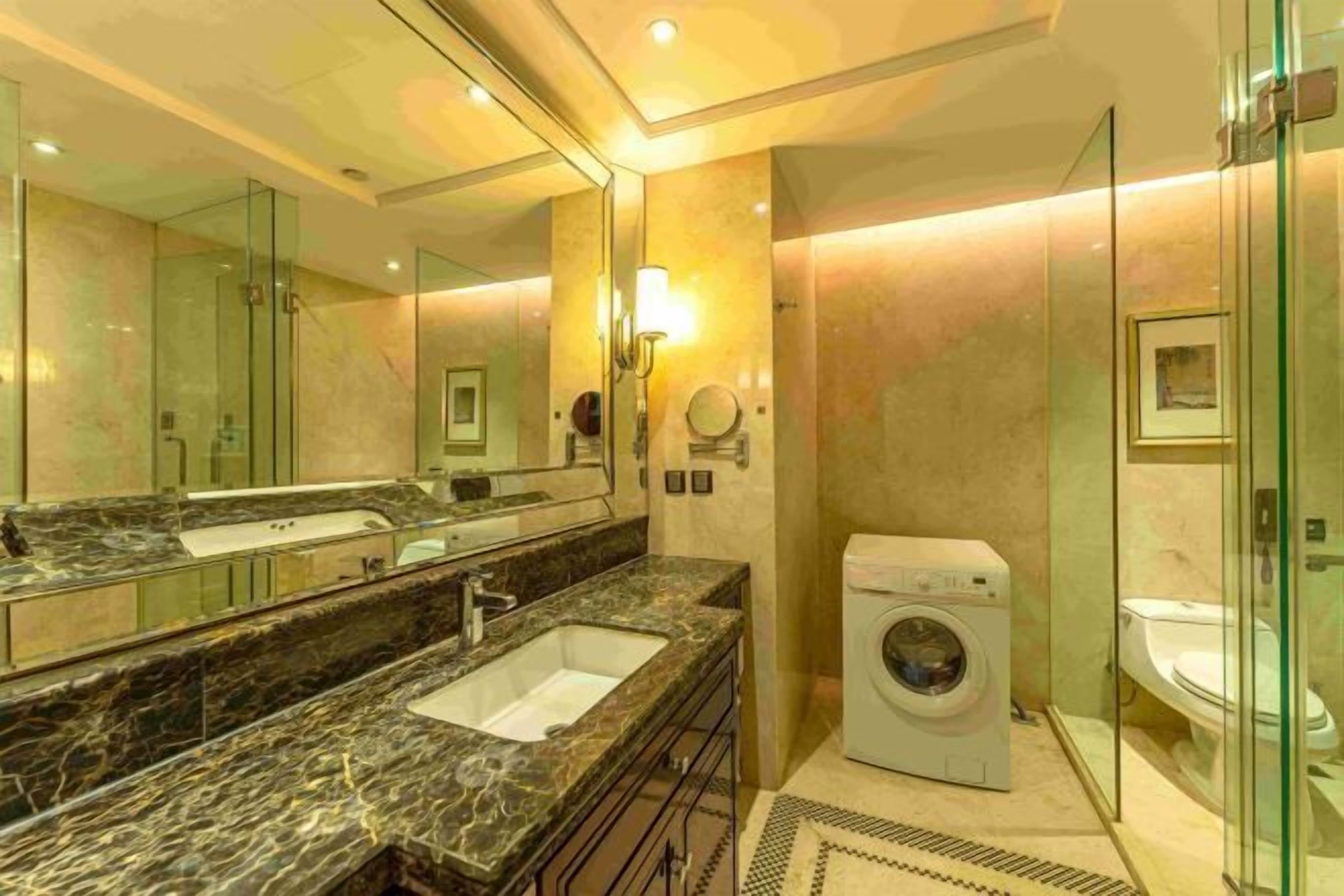 A modern bathroom with a marble sink, a washing machine, and a glass shower enclosure.