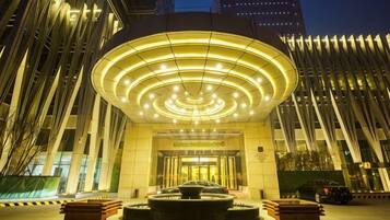 Entrada de un hotel con una lámpara circular, una recepción y una fachada de edificio moderna.