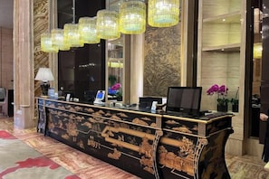 Una mesa de recepción con una computadora, un teléfono y un jarrón decorativo con flores.
