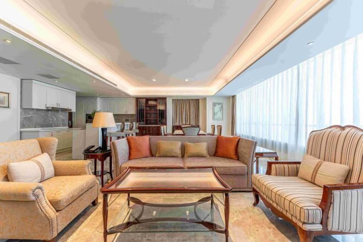 A modern living room with a sofa, armchairs, and a coffee table. There is a kitchen in the background.