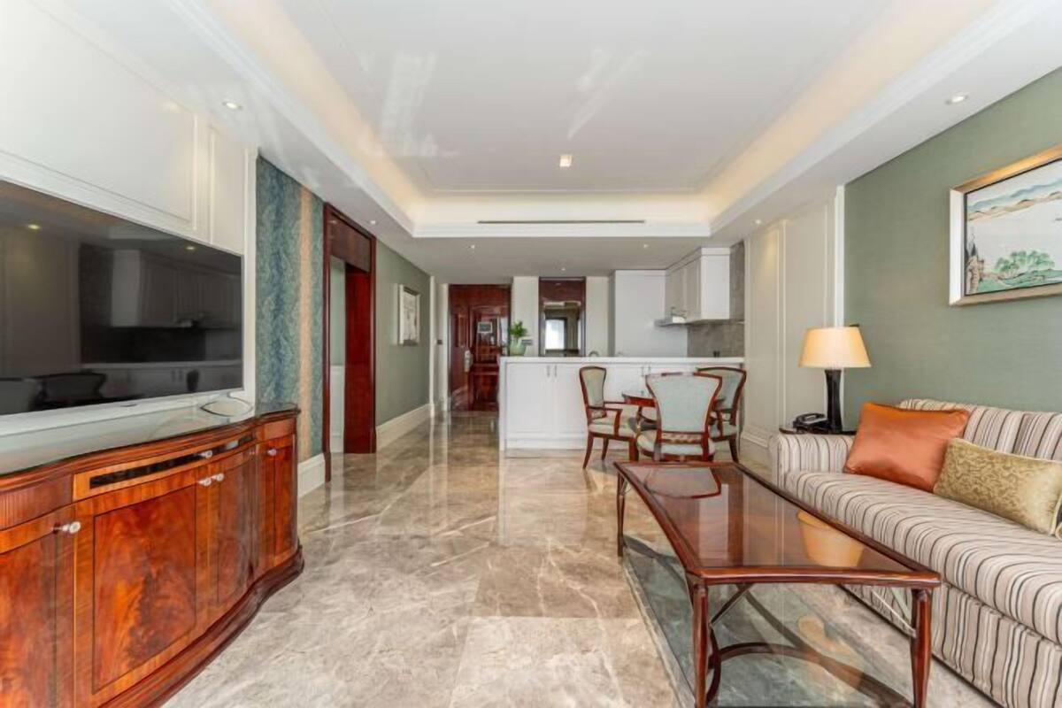 A spacious living area with a television, wooden cabinet, and a sofa with cushions.
