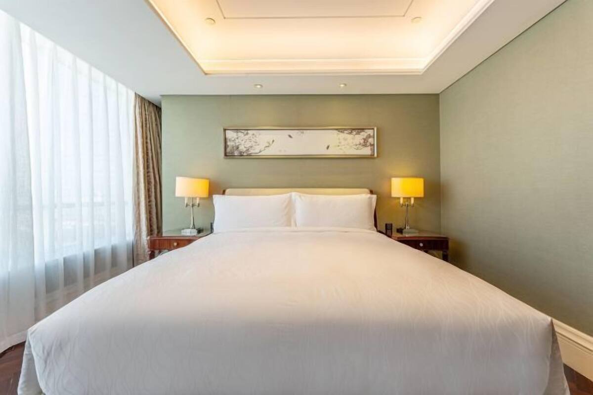 A hotel room with a large bed, two bedside tables with lamps, a ceiling light, and a painting on the wall.