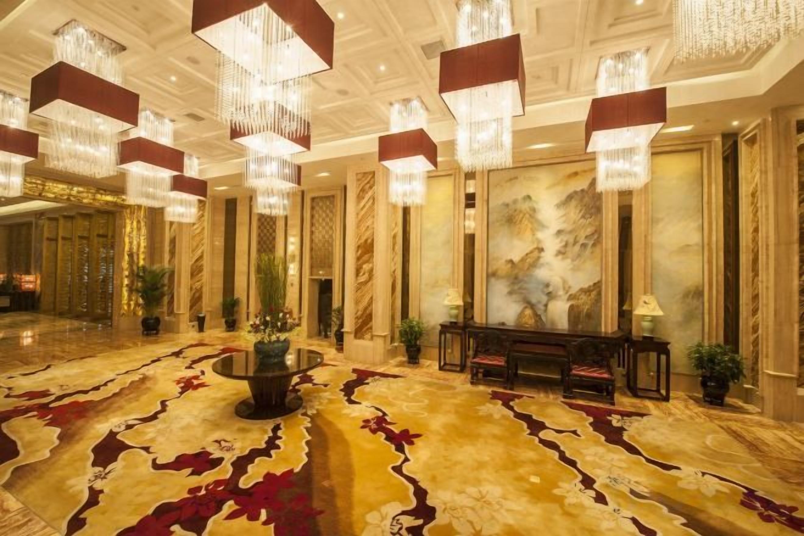 A spacious lobby with a patterned carpet, chandeliers, and a seating area with a table and chairs.