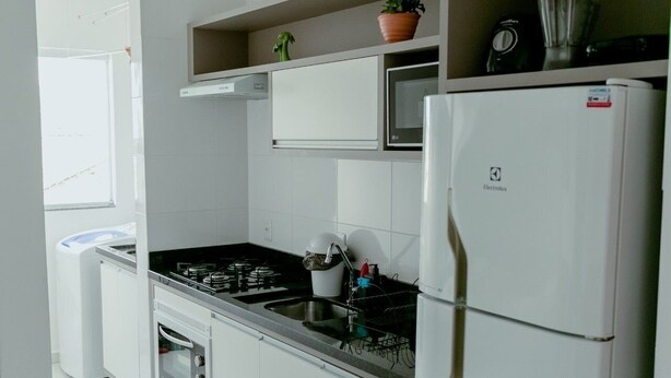 Een moderne keuken met witte kasten, een inbouwfornuis, een magnetron en een koelkast.