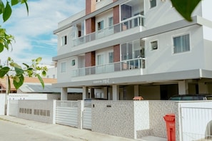 A multi-story residential building with a modern design, featuring balconies and a covered parking area.