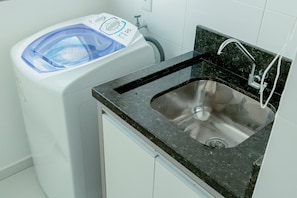 Cocina compacta con lavamanos integrado, lavadora y una pequeña encimera.