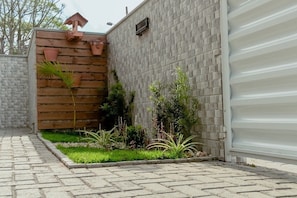 Un sendero pavimentado que conduce a una entrada con puerta de rejas, cerca de madera y plantas en macetas.