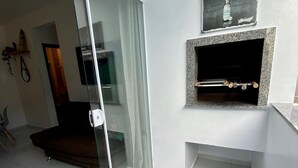 Een moderne woonkamer met een glazen schuifdeur naar een balkon, een open haard met een aangeplakte bierreclame, en een strakke, betegelde vloer.