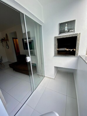 A modern living room with a glass sliding door leading to a balcony, a fireplace with a mounted beer advertisement, and a clean, tiled floor. - Residencial Diva (Florianópolis)