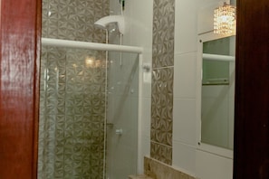 A shower with a geometric tile pattern, a glass door, and a light fixture above the mirror.
