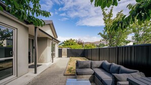A modern outdoor patio with a sectional sofa, a small table, and a covered area with sliding glass doors. - Calm at Leitrum - Cromwell Holiday Home (Cromwell)