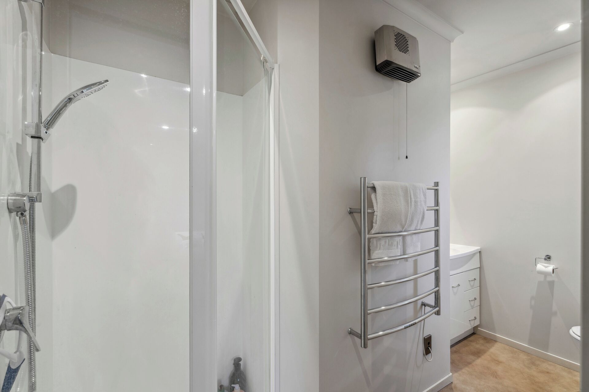 A modern bathroom with a glass shower enclosure, a towel rack, a toilet, and a wall-mounted air conditioner.