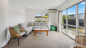 A modern living room with a grey sectional sofa, a wooden coffee table, and wicker chairs. - Calm at Leitrum - Cromwell Holiday Home (Cromwell)