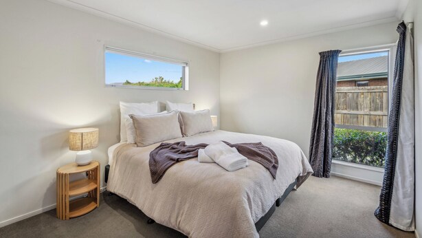 A bedroom with a bed, a bedside table with a lamp, a window with a view of greenery, and a curtain. - Calm at Leitrum - Cromwell Holiday Home (Cromwell)