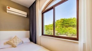 A hotel room with a bed, a window with a view of greenery, an air conditioning unit, and a curtain. - Zhujiajian Haiyu Seaview BNB (Zhoushan)