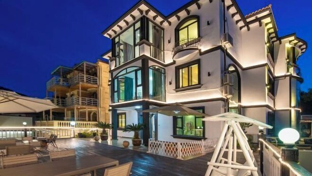 A multi-story building with balconies and large windows, featuring outdoor seating and a well-lit patio area. - Zhujiajian Haiyu Seaview BNB (Zhoushan)