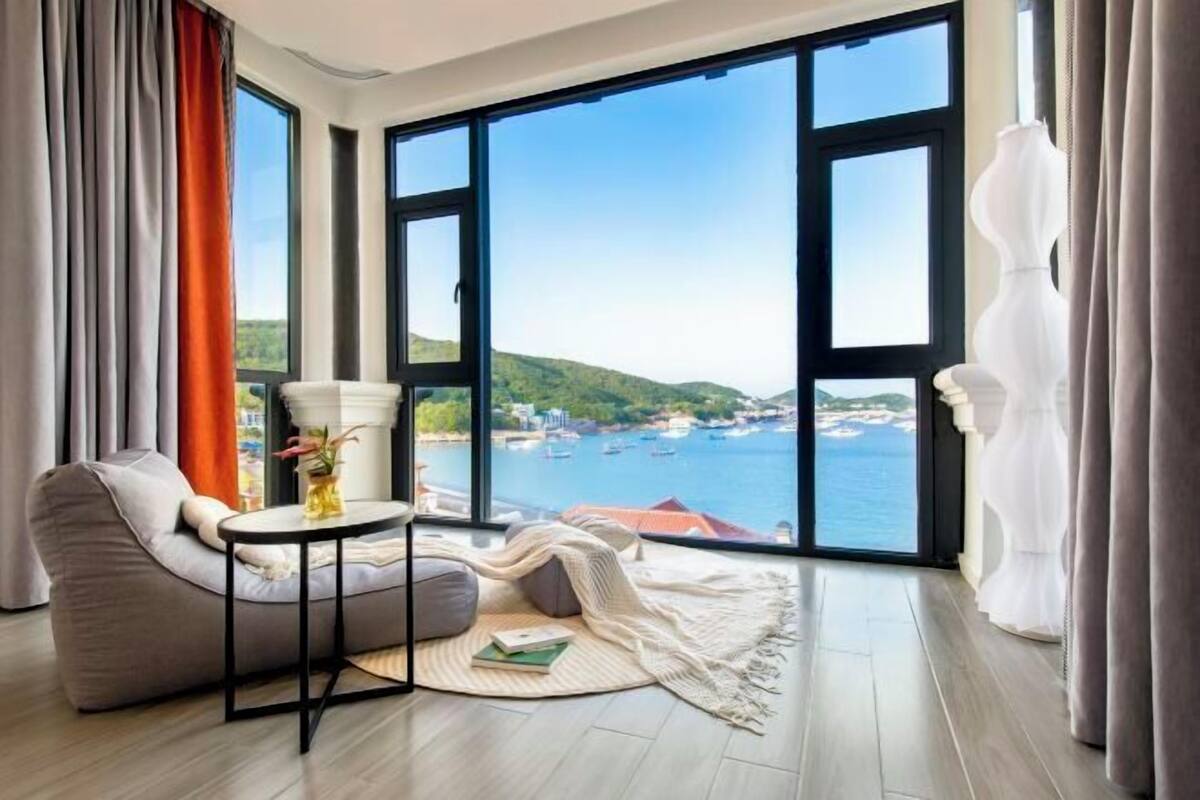 Ein Zimmer mit einem großen Fenster, einer Couch, einem kleinen runden Tisch und Meerblick.