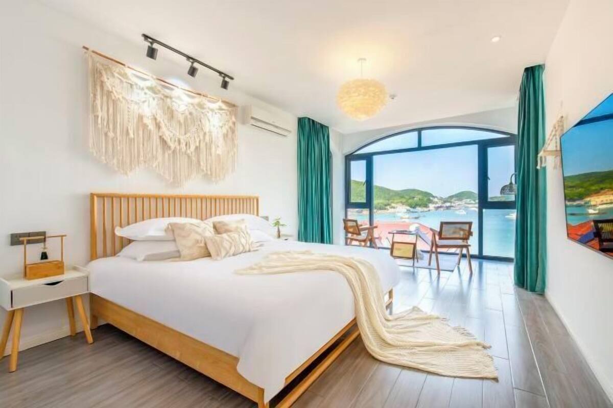 Ein Schlafzimmer mit Bett, Nachttisch und Blick nach draußen.