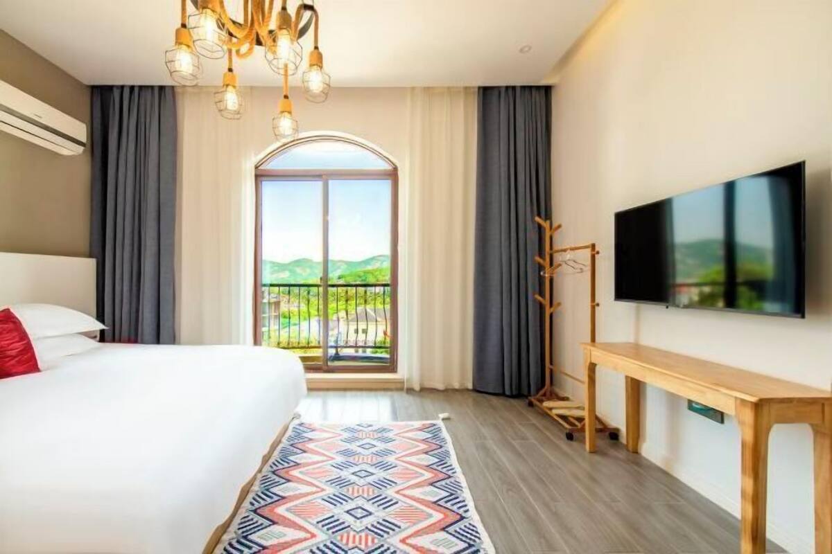 Ein Hotelzimmer mit Bett, Fernseher, Balkon und Blick sowie einem gemusterten Teppich.