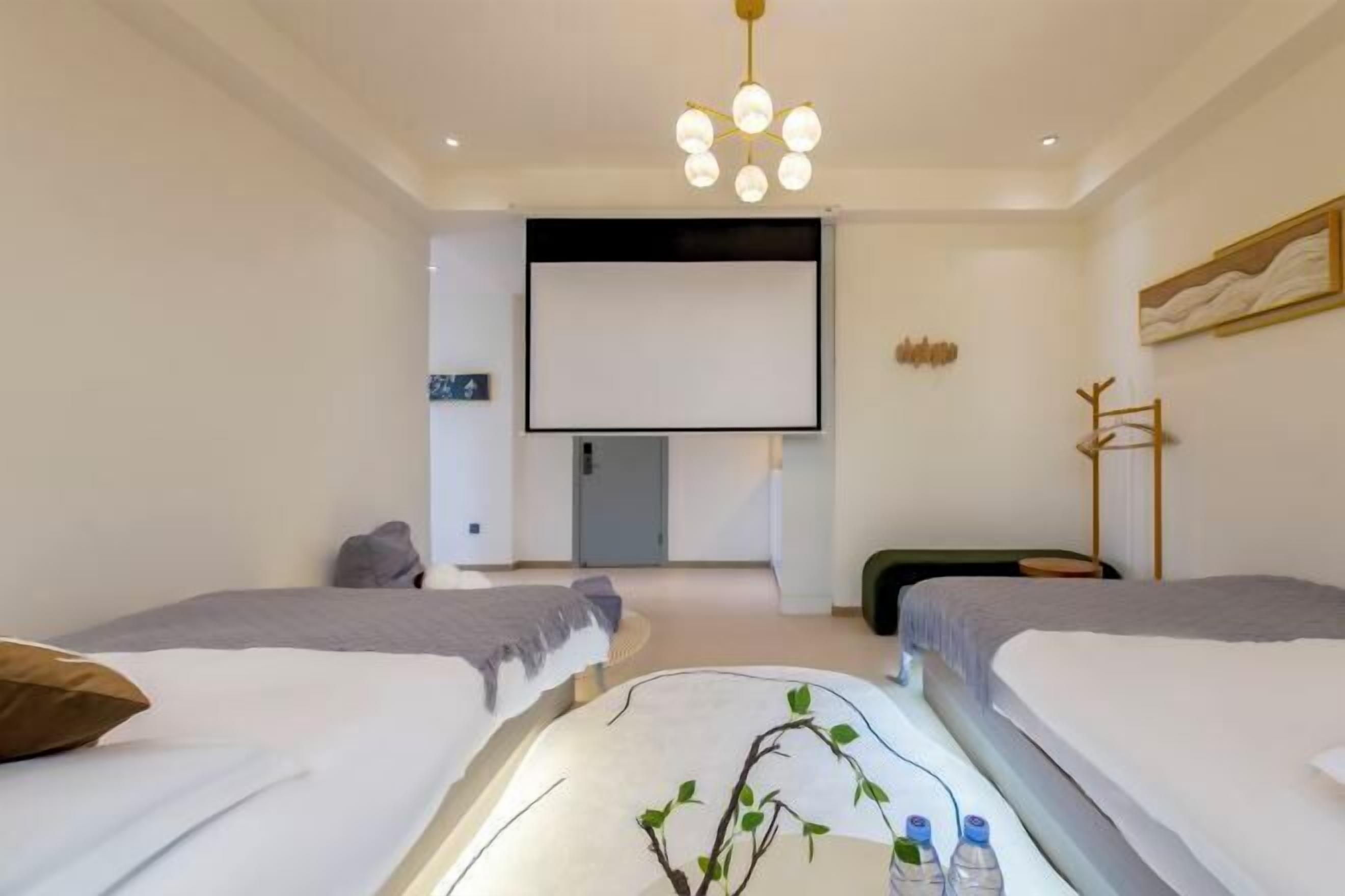 A modern hotel room with two beds, a flat-screen TV, a projector screen, and a ceiling light fixture.