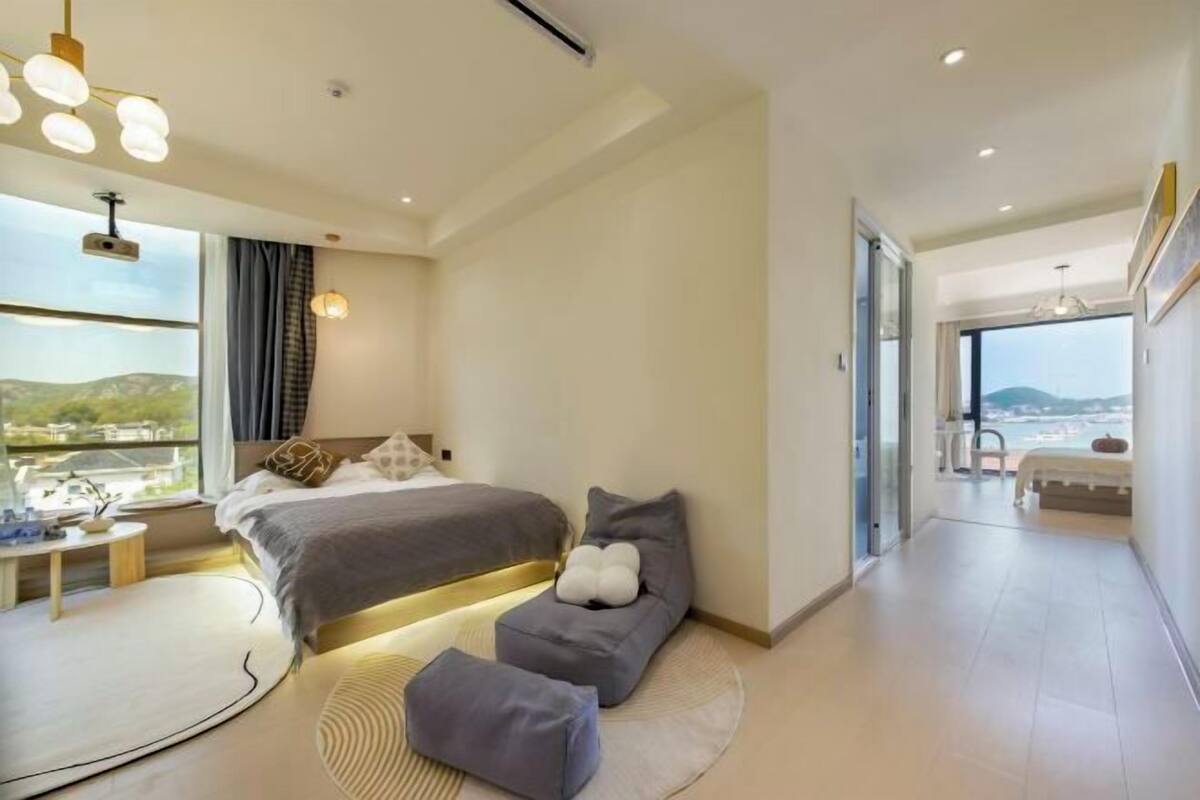 Ein modernes Schlafzimmer mit einem großen Bett, Nachttischen, Blick durch eine Glastür und einer kleinen Sitzecke.